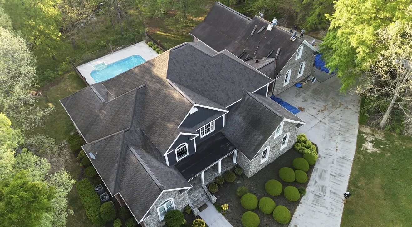 Completed shingle roof replacement on a large stone-and-siding home